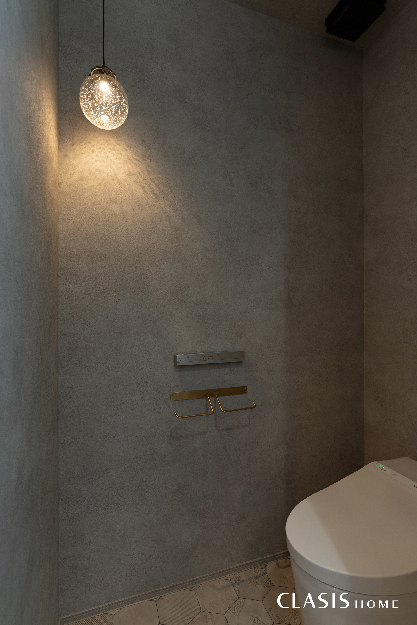 シンプルな壁紙と真鍮のペーパーホルダーが印象的なトイレ